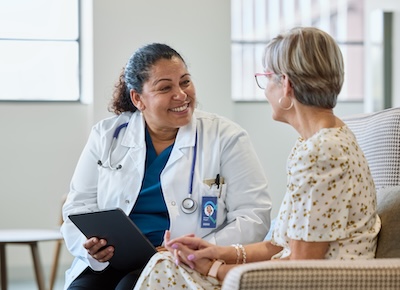 Smiling female physician sharing good news with senior woman at hospital. Doctor is consulting elderly patient.