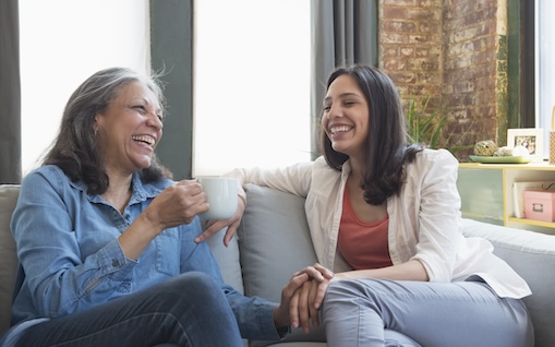 Hispanic mother and daughter laughing on sofa