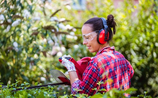 woman with hedge trimmer and wearing hearing protection